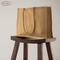 Pequena sacola de juta sobre uma mesa de madeira ao lado de uma planta frondosa, mostrando uma opção de sacola ecológica e biodegradável.